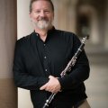 Paul Dean standing in a sandstone hallway holding a clarinet 